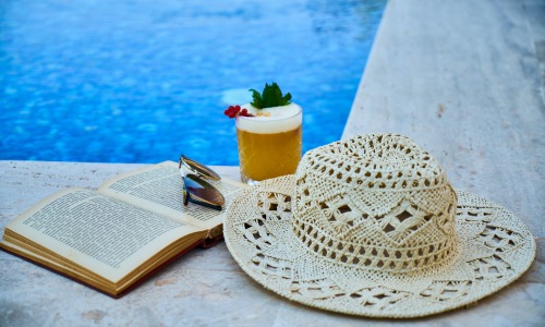 Open book, beverage, and hat by the pool