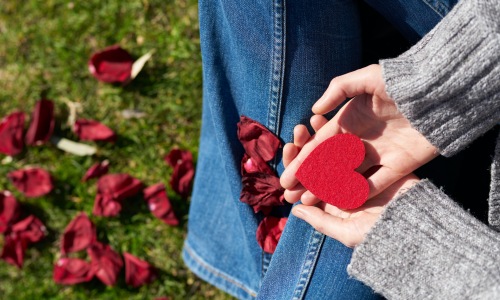 Woman sitting in park holding paper heart